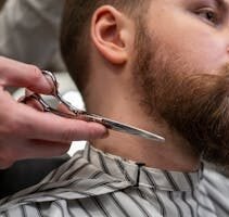 Detailed shot of a barber trimming a man's beard with scissors in a barbershop.
