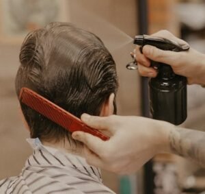 Hairdresser using a comb and spray bottle to style hair in a barbershop setting.